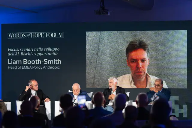 Liam Booth-Smith in collegamento da Londra sullo schermo della plenaria